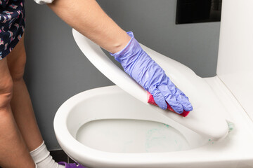 female hand in a blue glove wipes a white toilet bowl with a rag. House cleaning