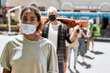 Young african american woman wearing mask waiting, standing in line, respecting social distancing...