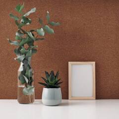 Wooden frame, vase with eucalyptus and houseplant in a pot, cork background. Mock up, copy space. Folk.