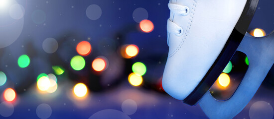 White ice skate shoe standing on the blade against the blurred Christmas lights. Copy space. Ice skating in the night rink. Winter holidays pastime activity - obrazy, fototapety, plakaty