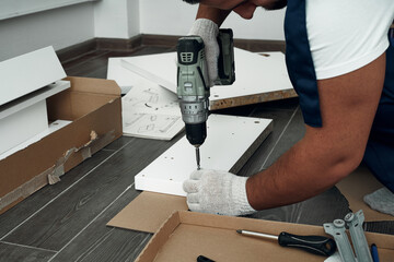 Furniture assembly process. Worker in overalls and white footwear. Using a cordless drill, screwdriver. Do it yourself.