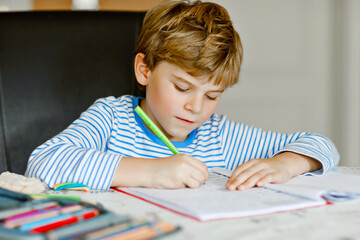 Portrait of cute healthy happy school kid boy at home making homework. Little child writing with colorful pencils, indoors. Elementary school and education. Kid learning writing letters and numbers