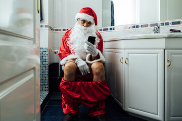 Santa Claus in the bathroom, sitting on the toilet pooping and looking at his cell phone