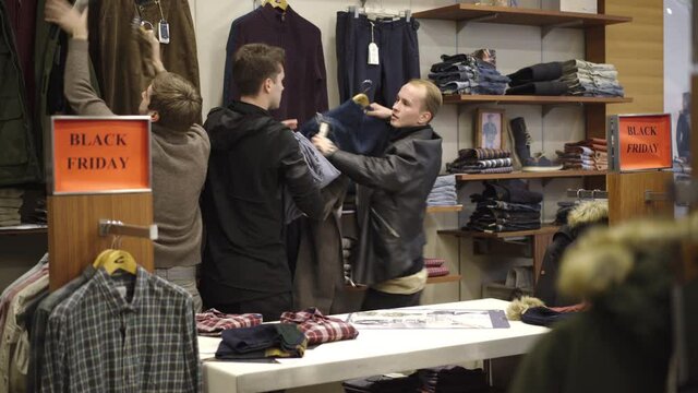 Rushing people taking clothes in shop on black friday. Group of clients hushing to get the best offer during sales in shopping mall. Men and women picking hangers. Shopaholism and consumerism.