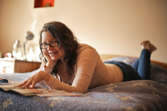 woman lying on the bed at home looks at a magazine