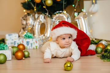 Obraz na płótnie Canvas Cute smiling baby is lying under a festive Christmas tree and playing with gifts. Christmas and New Year celebrations