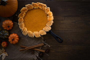 Homemade pumpkin pie baked in cast iron pan, on wooden background