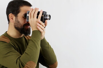 A man in a casual shirt on a white background is shooting with an 8mm camera turned sideways. Vintage concept