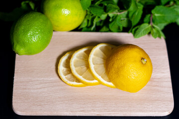 On a light wooden Board are slices of sliced fresh lemon. Next whole fruits with mint leaves on a...