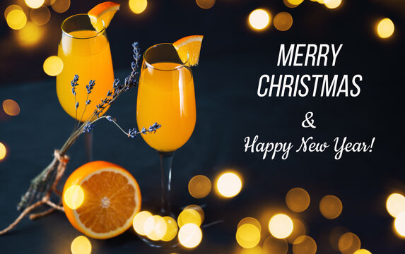 Mimosa cocktail on a dark background with baque garlands, merry Christmas greetings and happy new year text