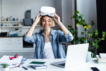happy woman taking off vr headset and looking at laptop