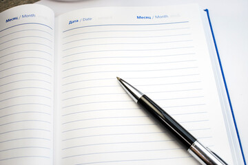 There is a black pen on a clean and empty open Notepad with lines on it.