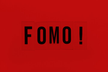 Abbreviation word FOMO on transparent plastic on red background. It means Fear Of Missing Out, non-stop internet surfing. Concept social communication problem between people, digital detox. Flat lay