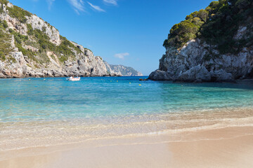 Empty beach of Agios Spyridon bay  in Corfu island in Greece, surrounded by rocks on a sunny holiday day. At sea, you can see a motorboat with tourists.