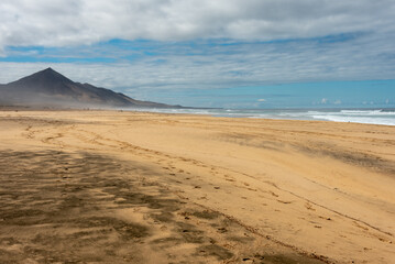 Famous Cofete Beach, known as Playa de Cofete, Fuerteventura, Canary Islands. Wide yellow sand under blue sky. High mountains in the background. Selective focus. 