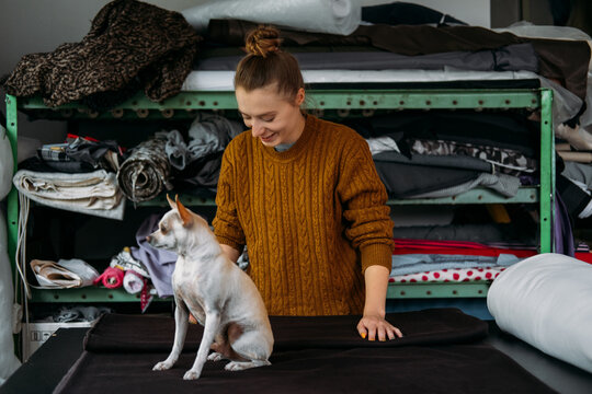 Small business, Fashion designer workplace, Tailoring Shop. Fashion Designer with pet dog Working In Her Studio. Beautiful female designer working in atelier with fabrics