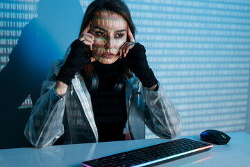 Internet, crime, cyber attack, system breaking concept. Blue neon light background. Woman hacker is working on a code with digital interface all around.