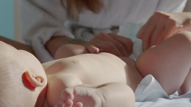 Mom changes diaper baby at night. Beautiful caucasian girl mother changes diaper to her little child. Close-up.