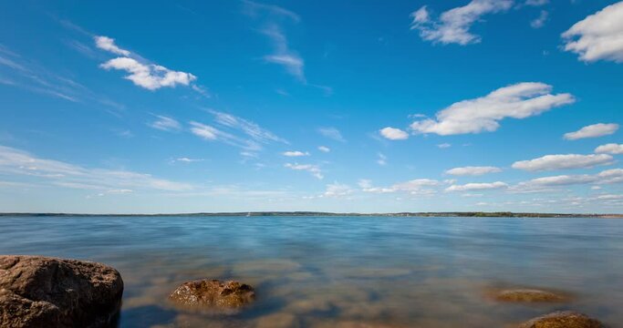 Time lapse of clouds forming over a lake. View through stones in the water.