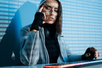 Internet, crime, cyber attack, system breaking concept. Blue neon light background. Woman hacker is working on a code with digital interface all around.