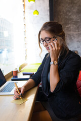 Female in fashionable glasses skilled economist talking with partner via mobile phone while sitting...