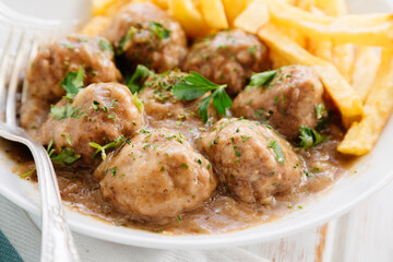 Close up of meatballs in sauce with parsley and fries