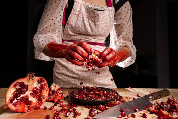 Woman with bloody or dirty hands removing the seed of a pomegranate.