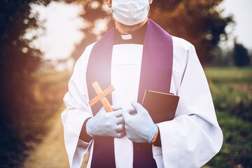 Man priest with a cross in a protective glovesa and medical mask .
