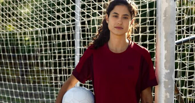 Confident female goalkeeper looking at camera by soccer net