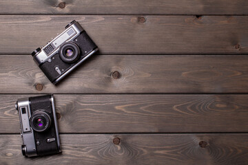 the lens up two vintage cameras stand against a background of brown wooden planks with space for copying