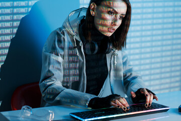 Internet, crime, cyber attack, system breaking concept. Blue neon light background. Woman hacker is working on a code with digital interface all around.