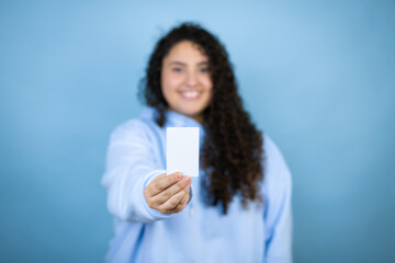 Young beautiful woman wearing casual sweatshirt over isolated blue background smiling and holding white card