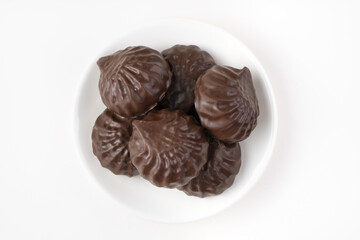Chocolate marshmallows are placed in a white plate on a light background. The view from the top. The concept of sweet food.