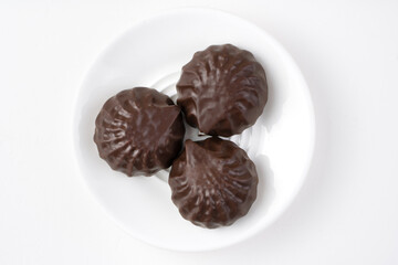 Three marshmallows covered with icing in a white plate on a light background. The view from the top. The concept of sweet food.