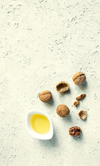 A white bowl with walnut oil and several walnuts on a gray background, olive oil alternative with unique flavor, top view with copy space