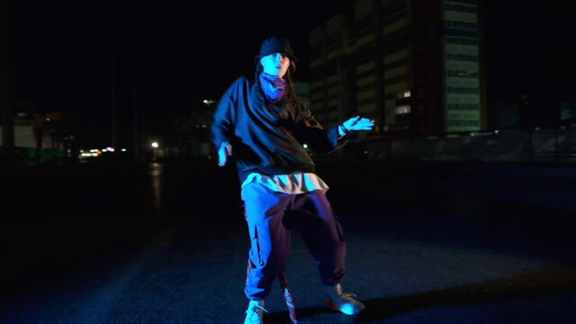 Cheerful young woman dancing hip hop, freestyle at night on a city street. Gimbal shot