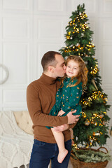 Little girl with her father near fir-tree. Christmas celebration. Girl with Dad weared in green and brown clothes. New year eve