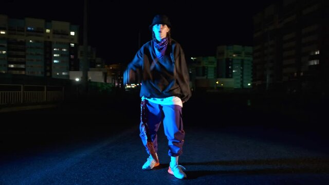 Stylish young woman dancing hip hop, freestyle or swag at night on a city street. Gimbal shot
