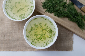 Two cups with vegetable broth are on the table, vegetables lie next to it, light, vertical photo