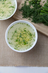 Two cups with vegetable broth are on the table, vegetables lie next to it, light, vertical photo