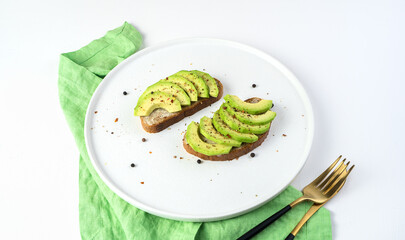 Diet sandwiches in a white plate on a light background. Slices of fresh avocado on bread. The concept of natural products.
