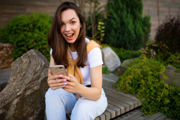 charming free young woman in casual look is drinking coffee while sitting in a summer park