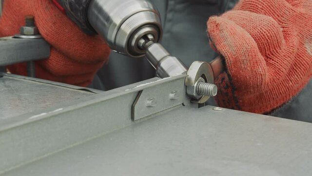 Closeup worker locksmith tightens nut with screwdriver closeup. The master tightens a nut metal plates on production.