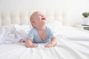 funny baby boy smiling and lying on a white bedding at home. 