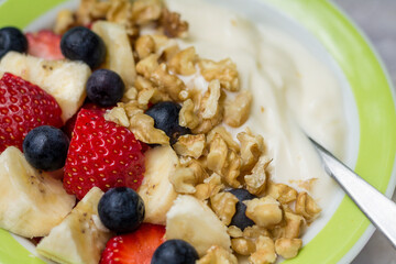 Closeup homemade healthy morning breakfast. Yogurt with fresh strawberries, blueberries, banana and nuts. Selective focus.