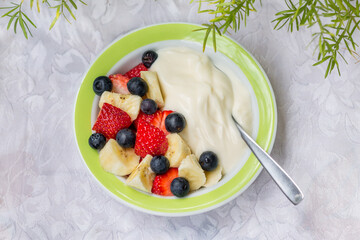 Healthy homemade breakfast bowl. Yogurt with fresh strawberries, blueberries and banana in a white backrgound with green plants border.