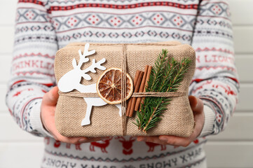 Delivery Man holding decorated gift box in eco-friendly reusable packaging. Man in sweater holds Christmas present. Close up
