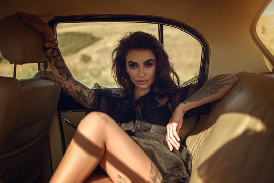 Gorgeous young dark haired woman half lying on the passenger seat of her retro car enjoying the sunlight