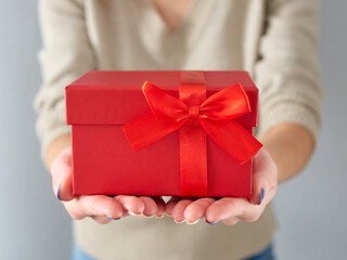 Female hands hold a red gift box. Birthday and Christmas gift with a red bow and ribbon. Giving a gift in a box. Time for gifts and Christmas.