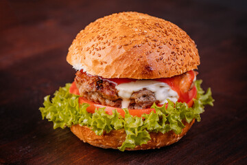 Beef burger with lettuce, tomatoes, slice of cheese,  and sauce on dark wooden background, close up